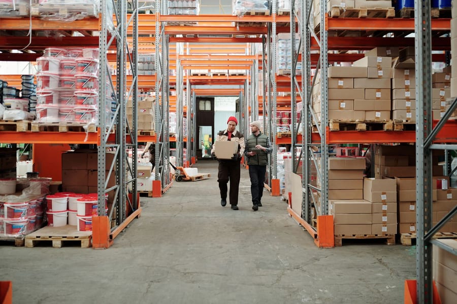 Two warehouse workers handling a package in an aisle